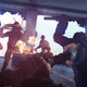 A player uses a melee weapon to attack a group of human enemies in a dark building near a fire.